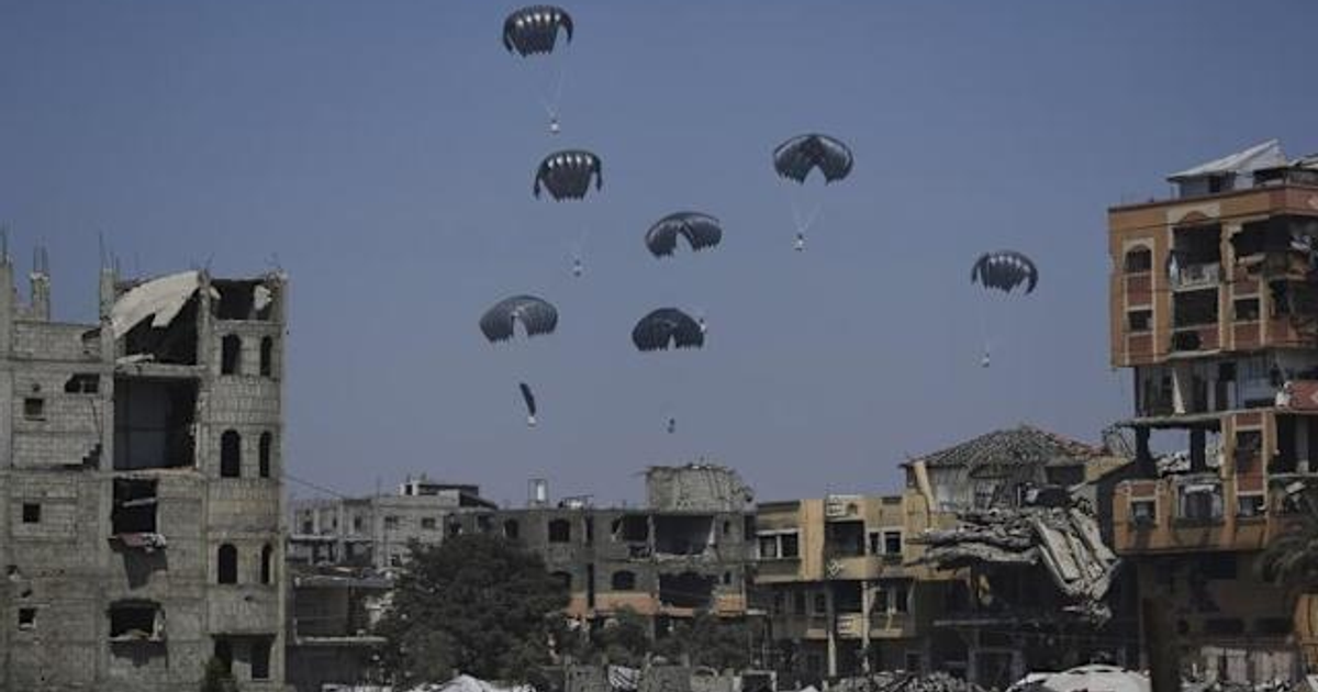 Paisaje urbano en ruinas con paracaídas descendiendo, representando una operación de ayuda humanitaria en Gaza.