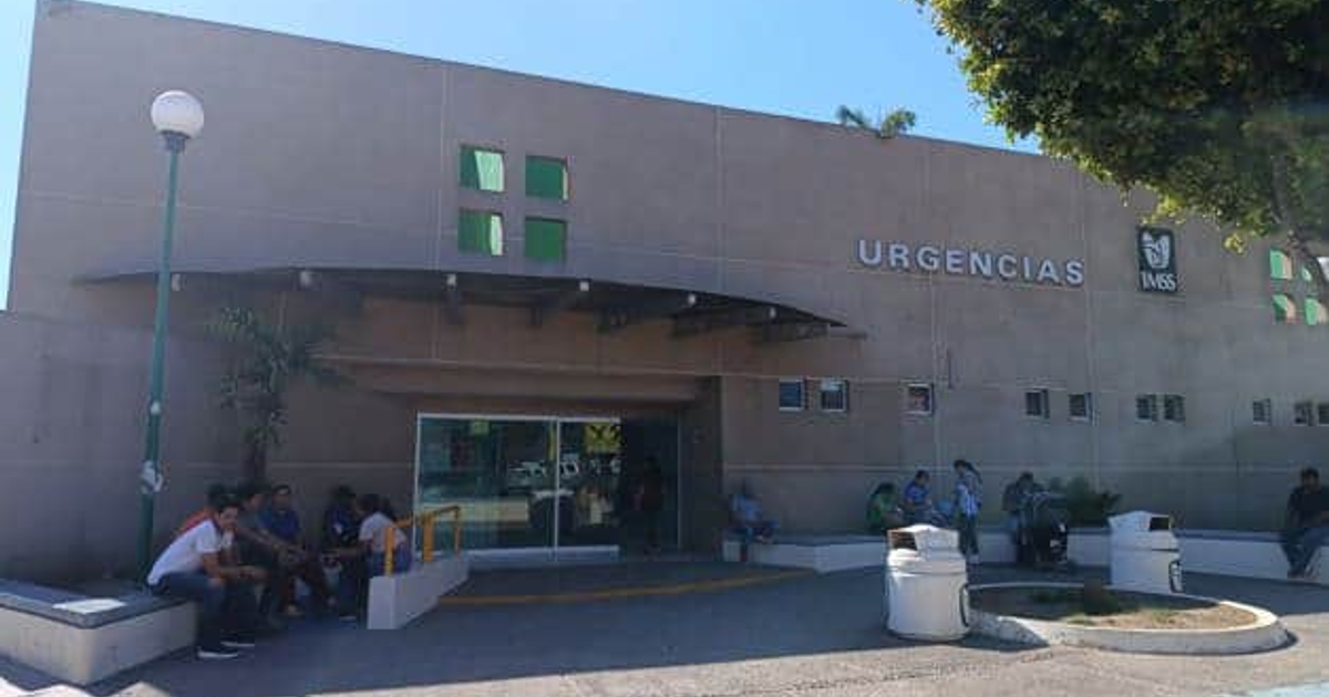 Entrada del área de urgencias del hospital del IMSS en Navolato con personas y mobiliario urbano.