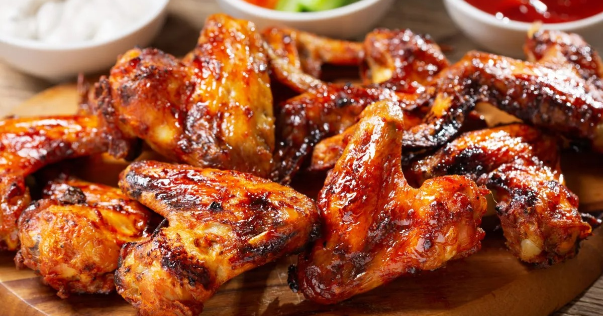 Alitas de pollo asadas doradas y glaseadas sobre madera con salsas de fondo