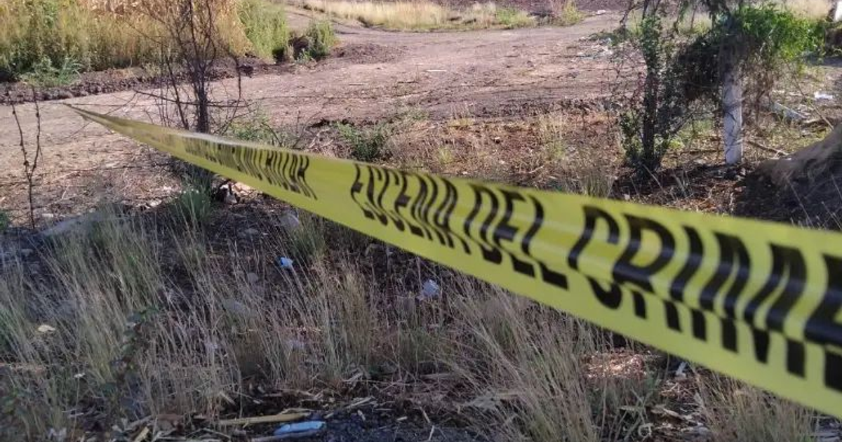 Cinta amarilla de escena del crimen en terreno rural con vegetación y basura.