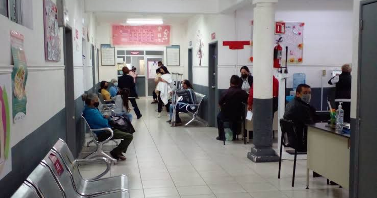 Interior de área de espera en clínica con personas sentadas y personal de salud al fondo