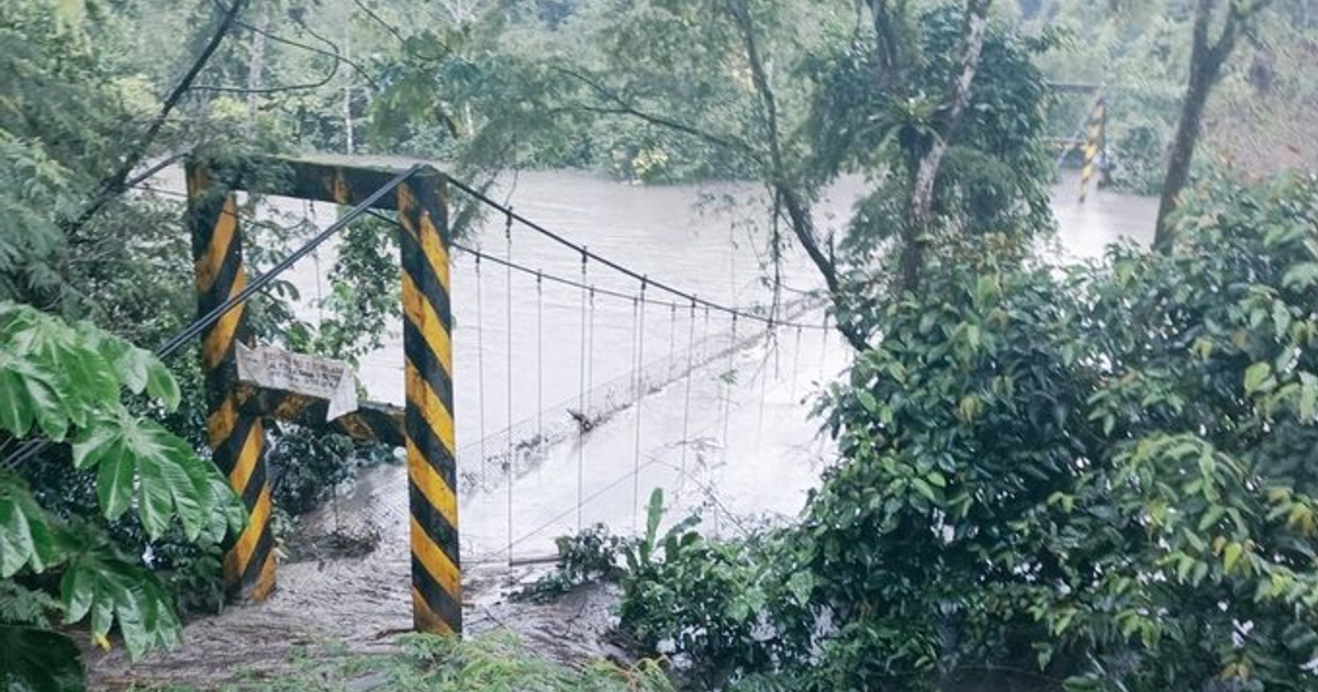 Puente colgante sobre río crecido con advertencias de seguridad