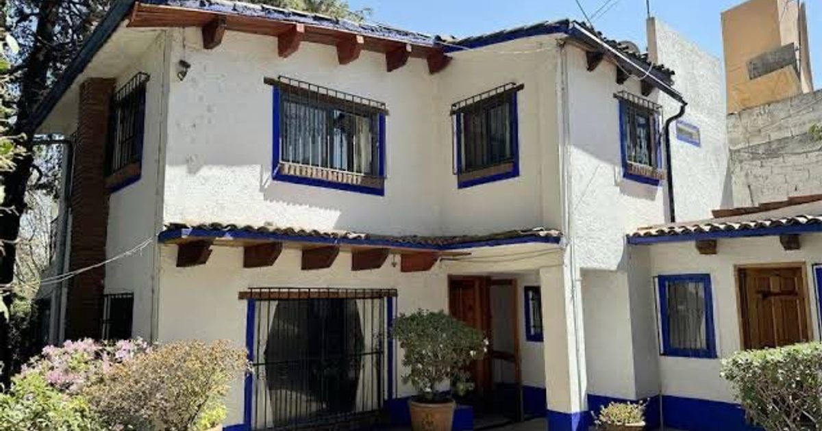 Casa de dos pisos en Tlalpan con paredes blancas y detalles en azul, rodeada de un jardín.