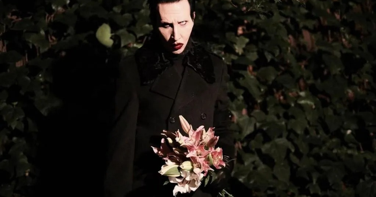 Persona con abrigo negro y ramo de flores frente a hojas verdes