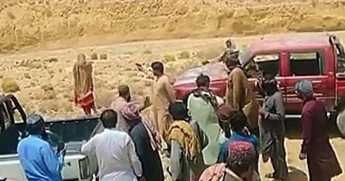 Grupo de personas en un paisaje árido con vehículos, relacionado con una ejecución pública en Baluchistán.