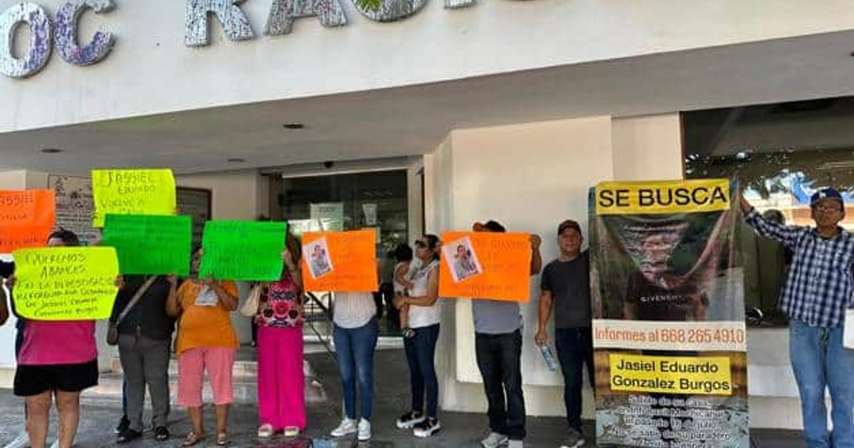 Protesta en Los Mochis por la desaparición de Jassiel Eduardo, con personas sosteniendo carteles frente a un edificio.