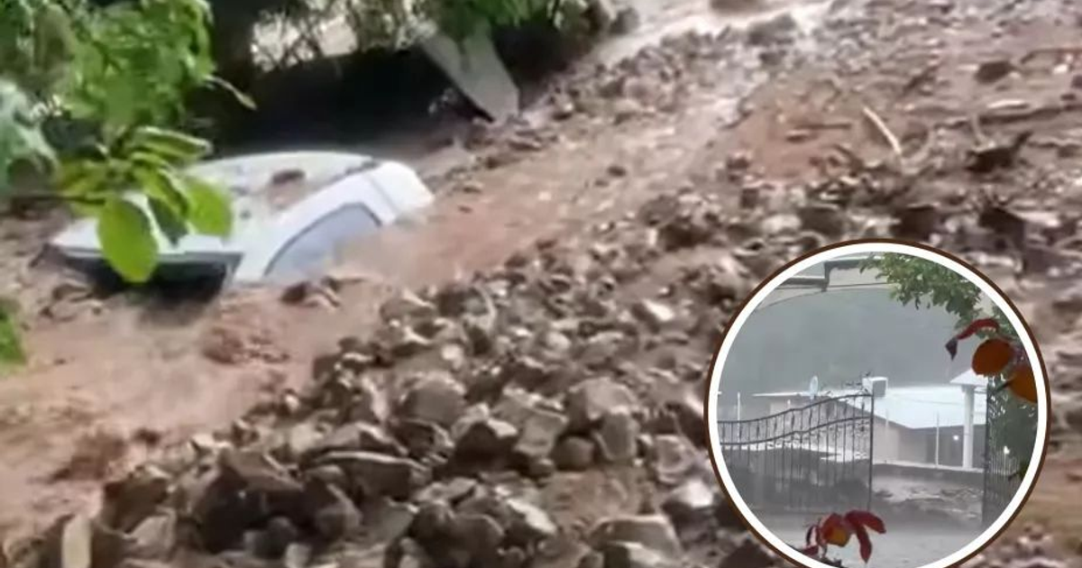 Paisaje afectado por deslizamiento de tierra en Potrero de la Vainilla, con vehículo atrapado y estructura en segundo plano bajo clima lluvioso.