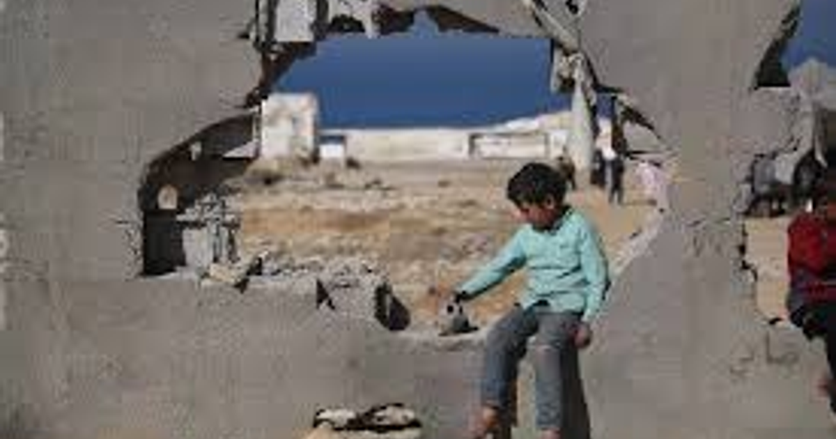 Niño sentado en un agujero en la pared, mirando un paisaje desolado en Gaza.