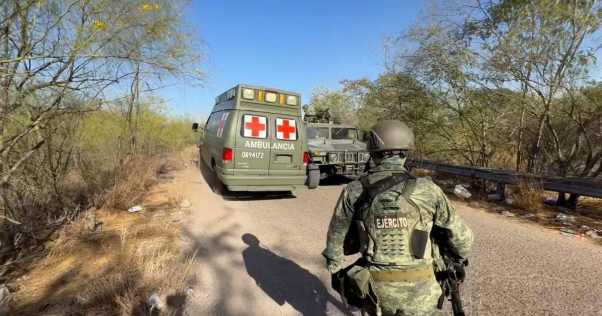 Ambulancia verde con cruces rojas junto a vehículo militar en camino árido