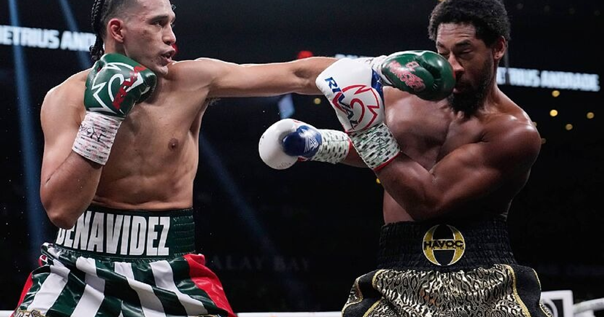 Dos boxeadores en el ring, uno lanzando un golpe y el otro defendiéndose, con público y luces de fondo.