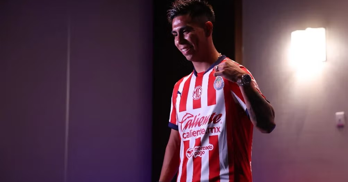 Efraín Álvarez sonríe mientras señala la camiseta de Chivas, destacando su nuevo rol en el equipo.