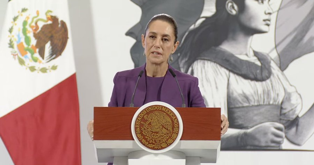 Mujer hablando en un podio con el escudo de México, bandera y mural de fondo.