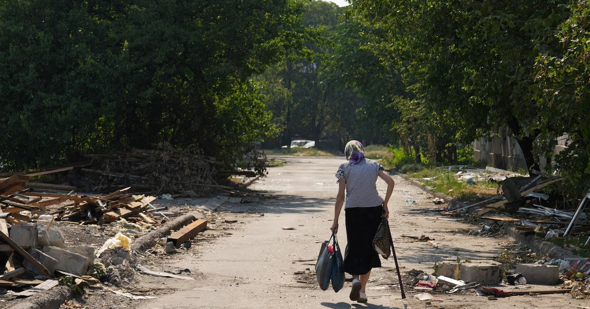 Mujer mayor caminando por una calle desierta en Dobropillia, rodeada de escombros y basura, simbolizando el desplazamiento forzado.