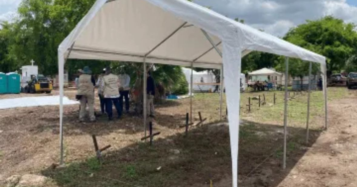 Carpa blanca en exhumación masiva en Culiacán con personas conversando y portacontenedores al fondo.