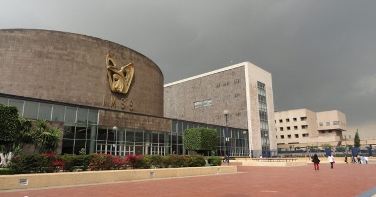 Edificio moderno del IMSS con vegetación y personas caminando, cielo nublado.