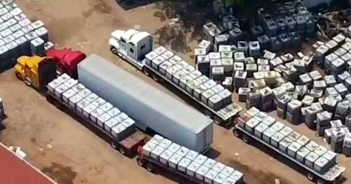 Vista aérea de camiones y contenedores en un área de carga, destacando un camión rojo y amarillo en el centro.