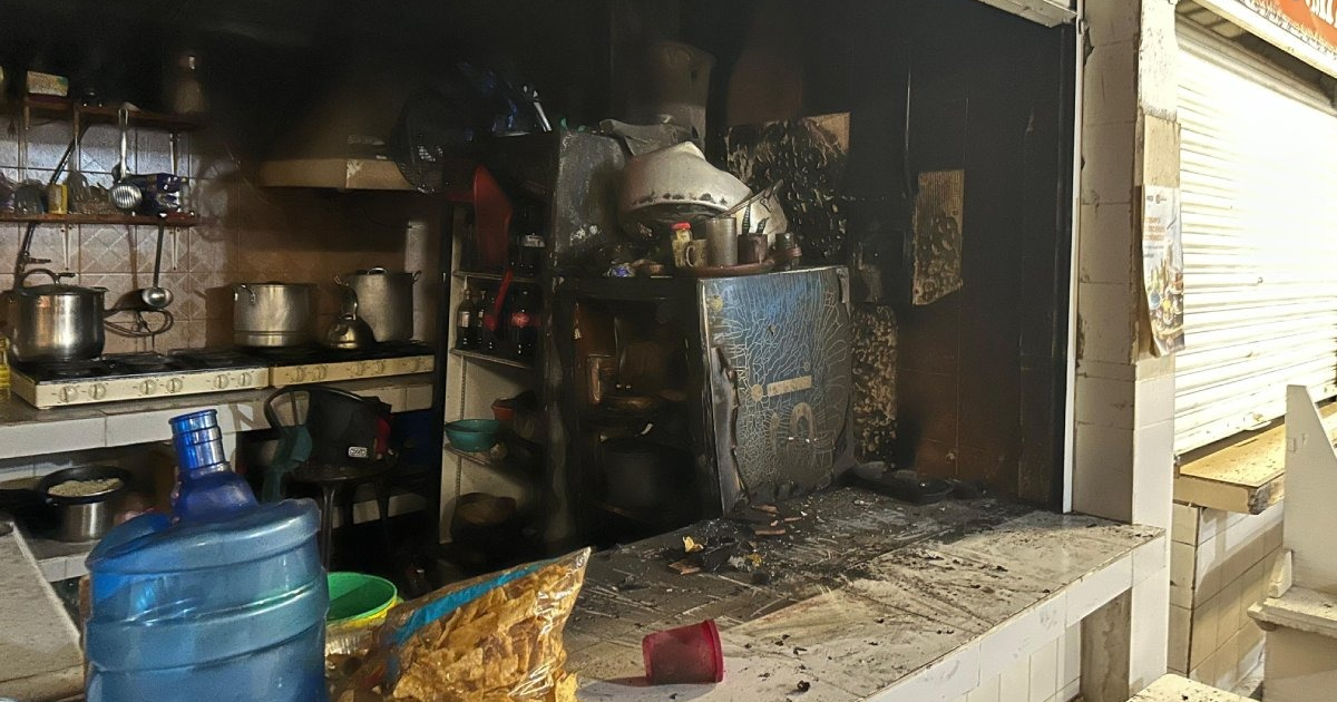 Cocina dañada por incendio en mercadito Independencia, Los Mochis, con utensilios y ollas en estufa, refrigerador quemado y ambiente oscuro por humo.
