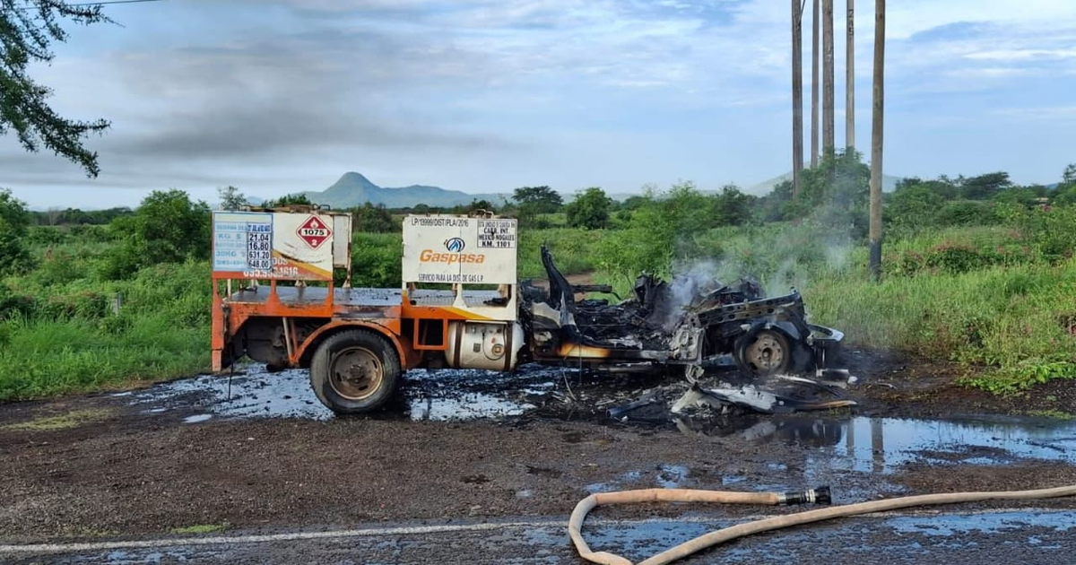 Vehículo quemado en carretera México 15, rodeado de vegetación y montañas, con tanque y manguera visibles.