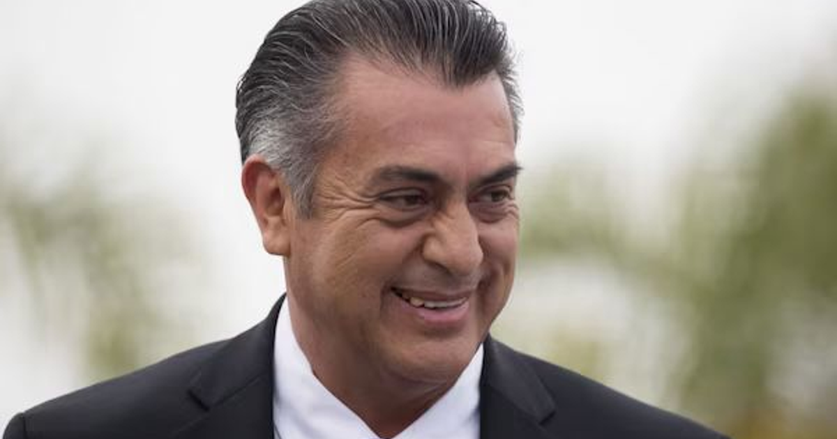 Hombre sonriente en traje oscuro con fondo al aire libre