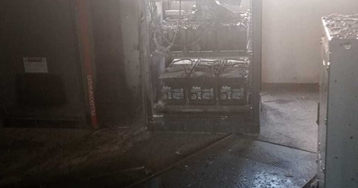 Subestación eléctrica con baterías desgastadas y cables visibles en un entorno polvoriento.