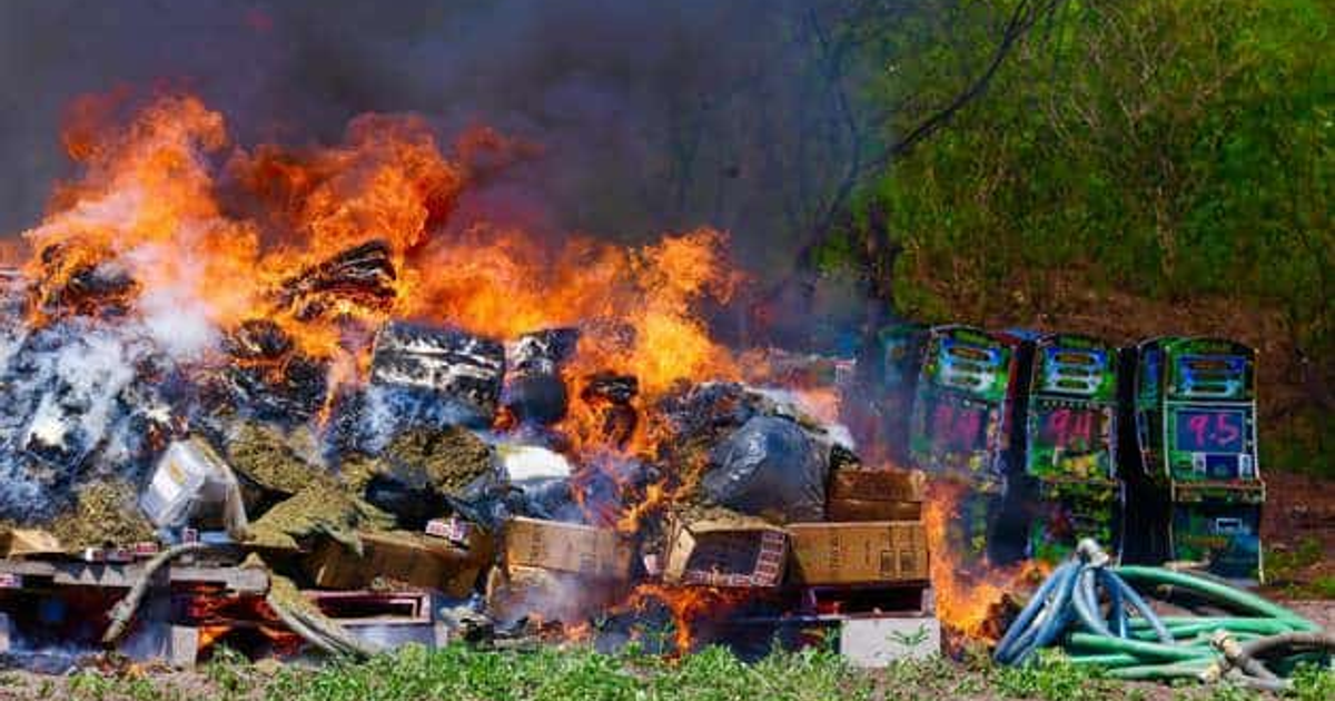 Hoguera con llamas y humo, rodeada de basura y máquinas tragamonedas durante incineración de narcóticos en Culiacán.