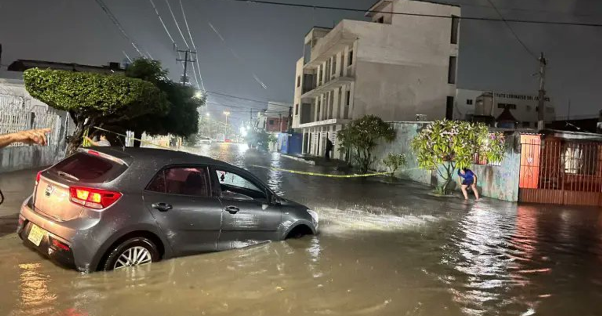 Inundación nocturna en Mazatlán con automóvil sumergido y persona sentada cerca de una pared.