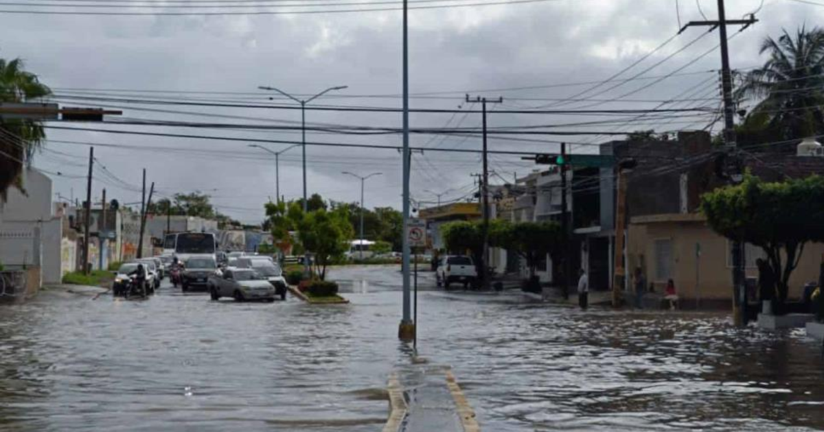 Calle inundada con vehículos sumergidos, edificios y cielo nublado tras intensas lluvias.