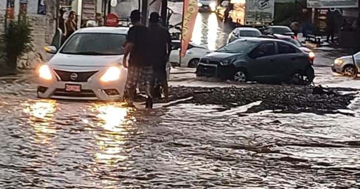 Calle inundada en Santa Elena con vehículos y personas afectadas por lluvias torrenciales
