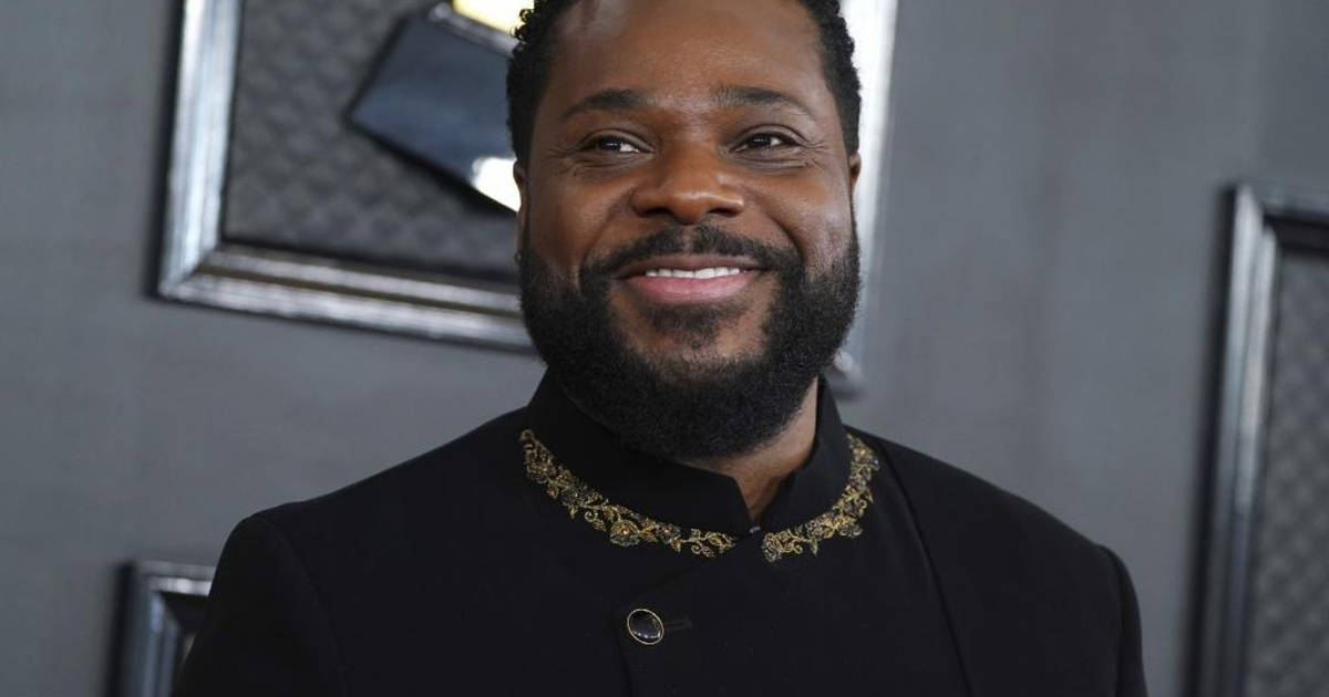 Hombre sonriente con barba y chaqueta negra en entorno elegante