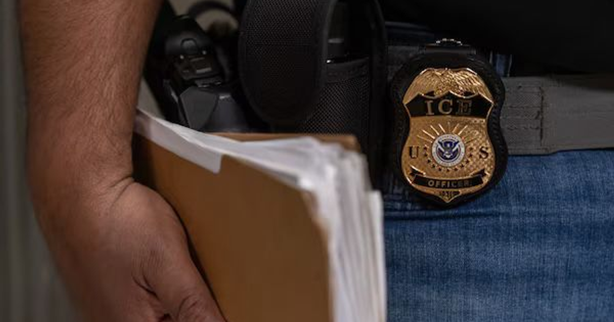 Agente de ICE sosteniendo documentos y equipo oficial