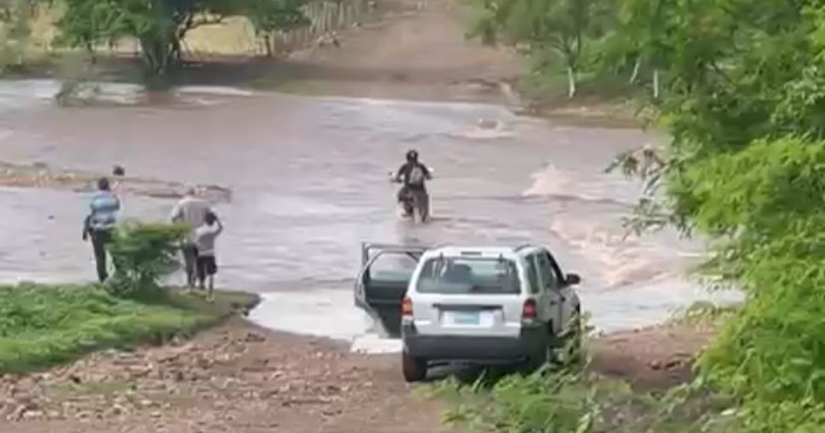 Motociclista cruzando arroyo crecido en Sinaloa, observado por personas en la orilla.