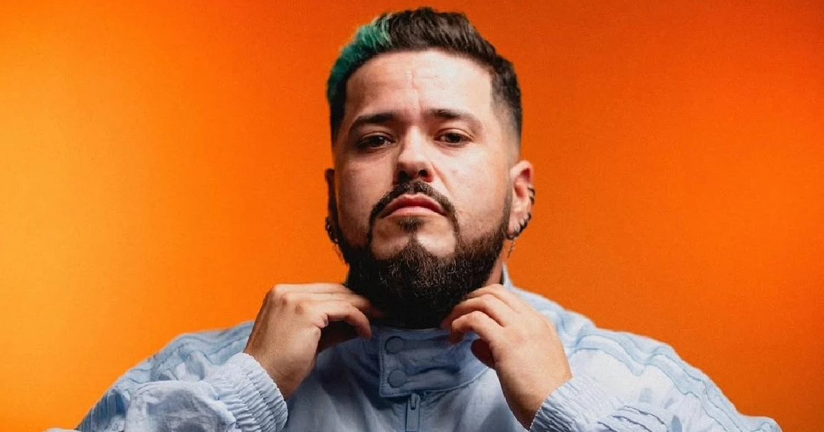 Persona con barba y chaqueta sobre fondo naranja, relacionada con la noticia del fallecimiento de Aldo Miranda.