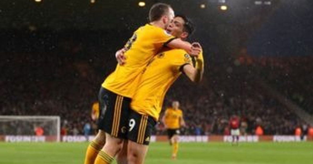 Dos jugadores de fútbol abrazándose en un estadio lleno de aficionados, ambos con camisetas amarillas.