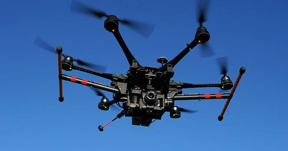 Dron negro con cámara volando en cielo azul, vinculado a la vigilancia de narcodrones.