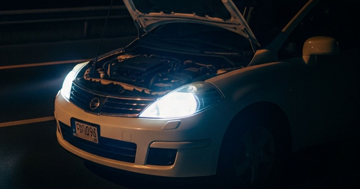 Automóvil blanco con capó abierto y luces encendidas en la noche