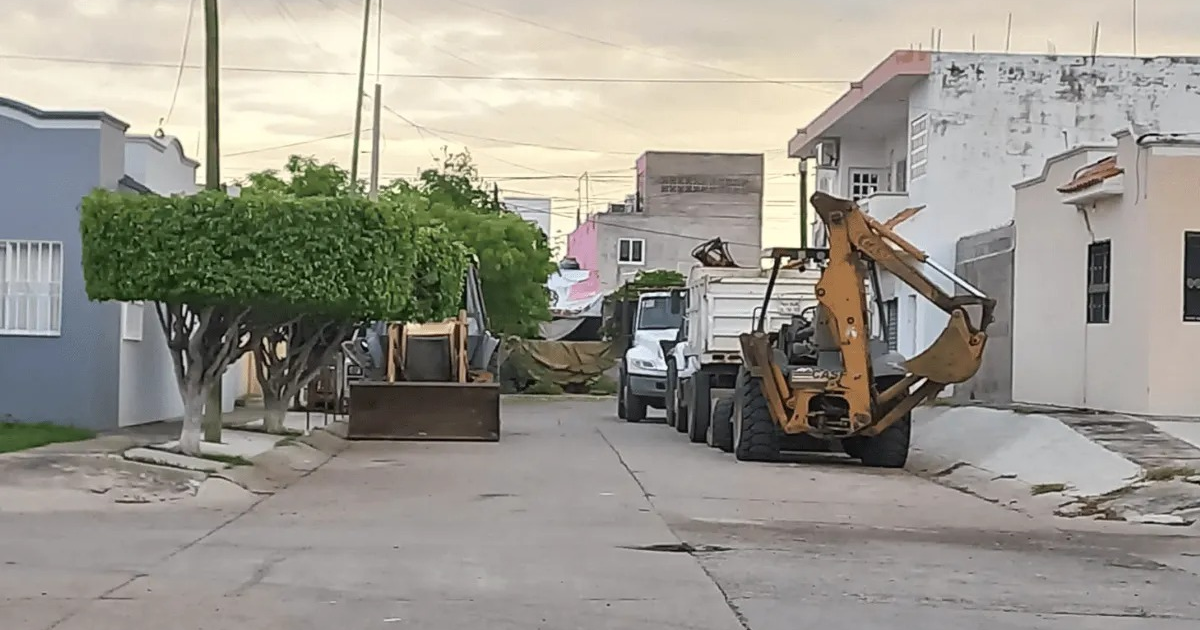 Calle urbana con maquinaria de construcción y vehículos en Prados del Sol, reflejando obstrucción vial.