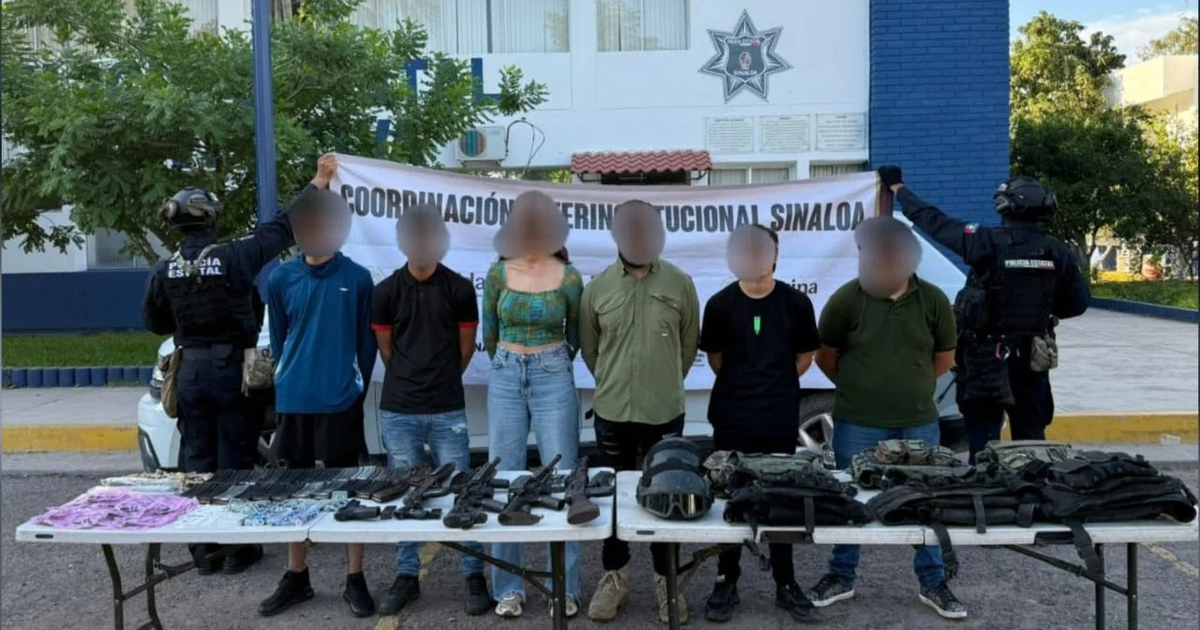 Personas alineadas frente a una mesa con armas y equipo táctico durante un operativo en Sinaloa.