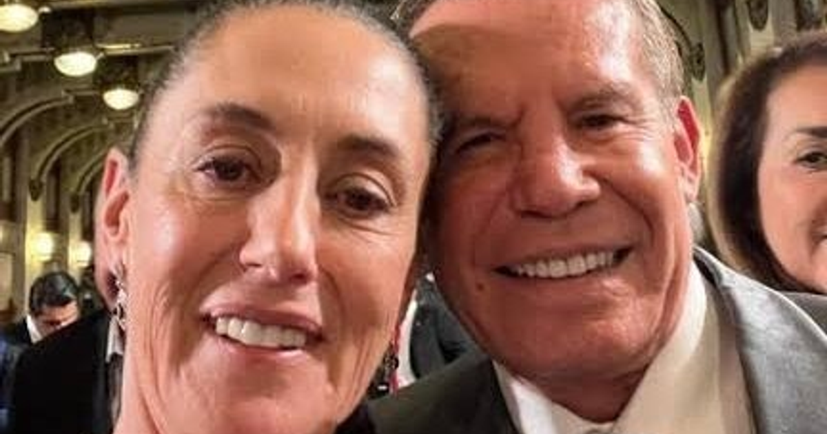 Dos personas sonriendo mientras toman una selfie en un lugar con luces y arquitectura elaborada.