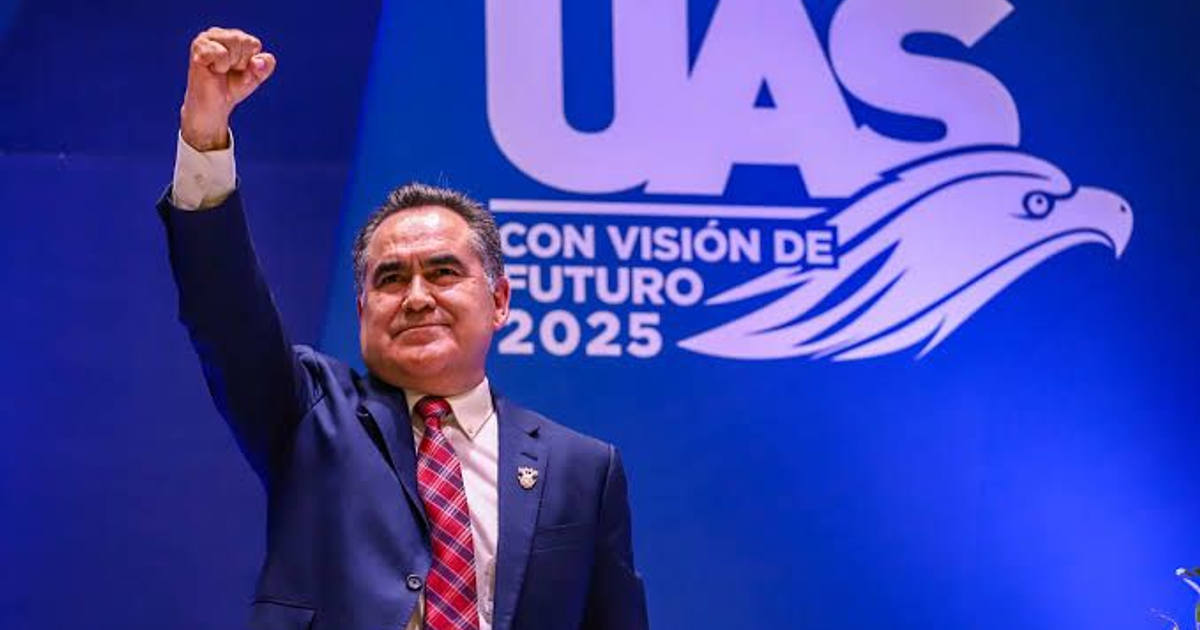 Hombre en traje oscuro levanta el puño en evento de la UAS con fondo azul y águila.