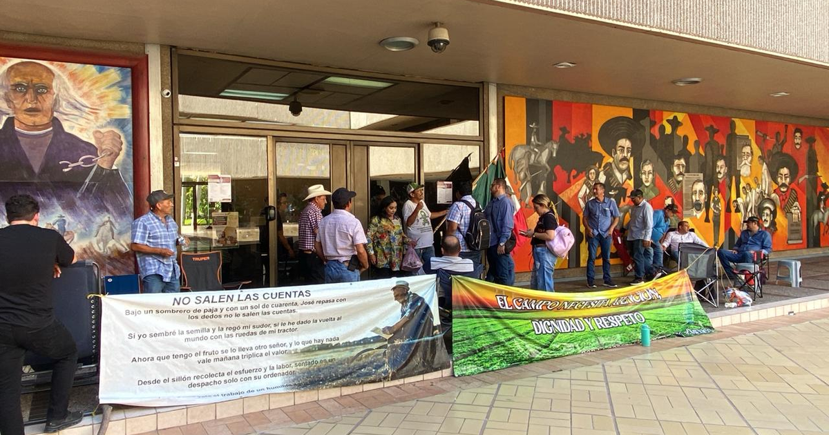 Agricultores protestan frente al palacio de gobierno en Sinaloa, con pancartas y un mural de fondo.