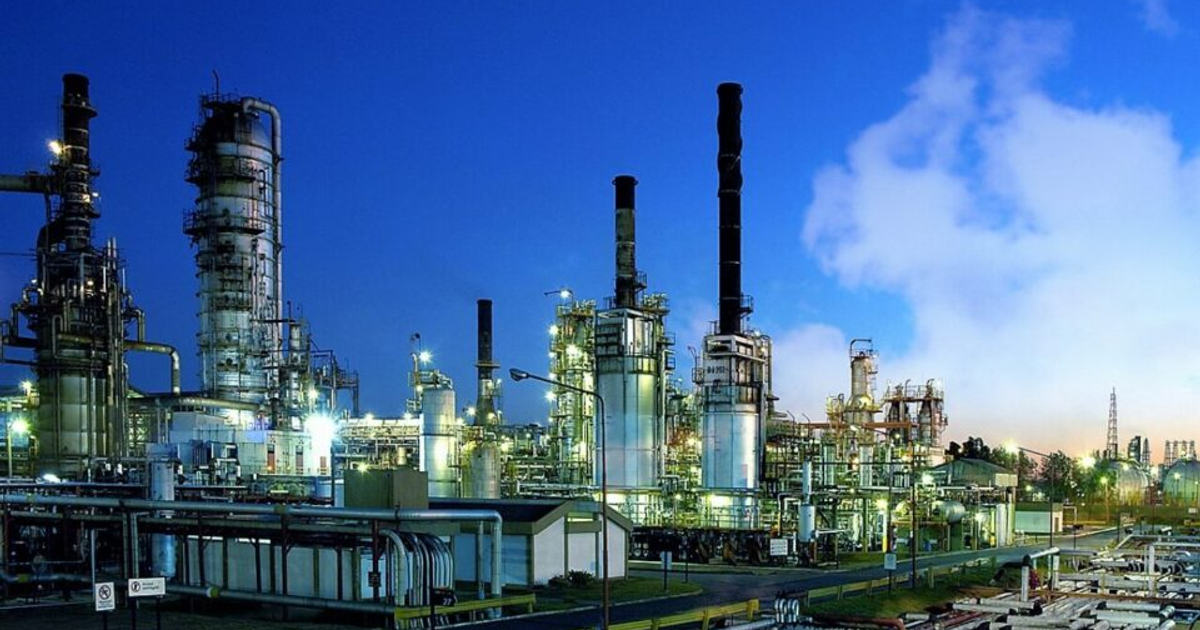 Refinería de metanol en Topolobampo al atardecer, con torres, chimeneas y luces encendidas.