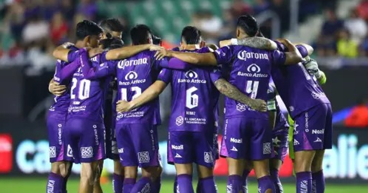 Jugadores del Mazatlán FC en círculo de motivación antes del partido, vestidos con uniformes púrpura en el campo de juego.