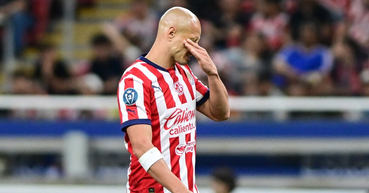 Jugador de Chivas con camiseta de rayas rojas y blancas mostrando frustración en el campo de fútbol.
