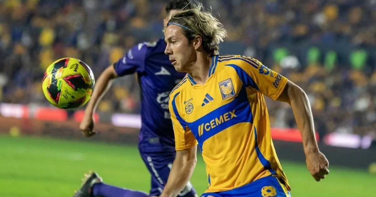 Sebastián Córdova en acción con camiseta amarilla y azul, persiguiendo un balón en el aire, con un estadio lleno de fondo.