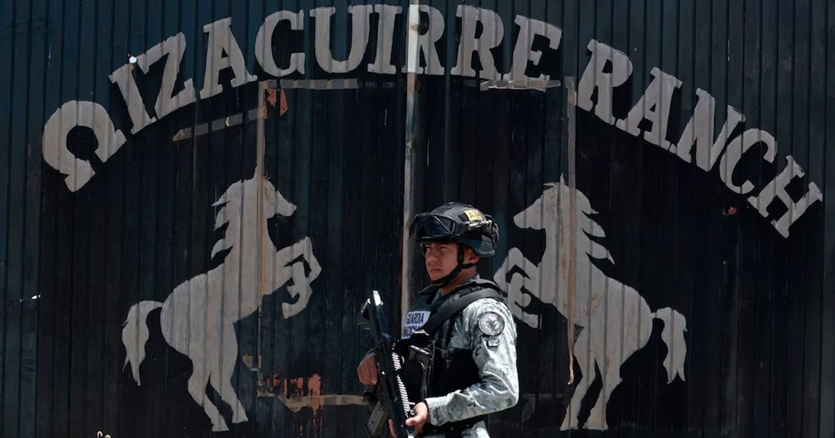 Oficial armado frente a la entrada del Rancho Izaguirre en Jalisco, con siluetas de caballos en la puerta.