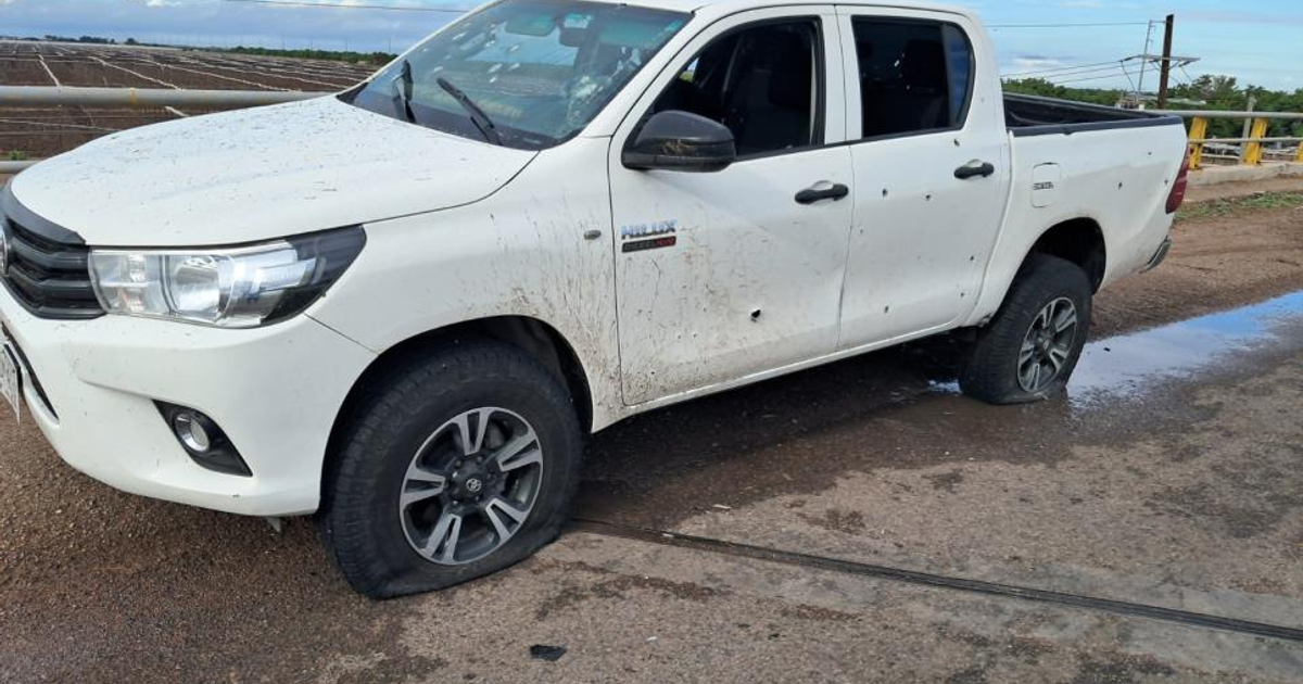 Camioneta Toyota Hilux blanca con neumático desinflado y marcas de impacto en un paisaje agrícola.
