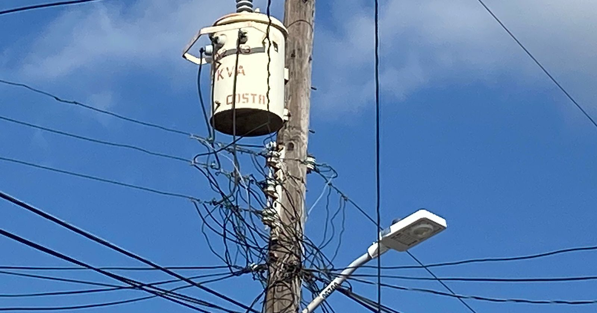 Poste de electricidad con transformador y cables enredados bajo un cielo azul.