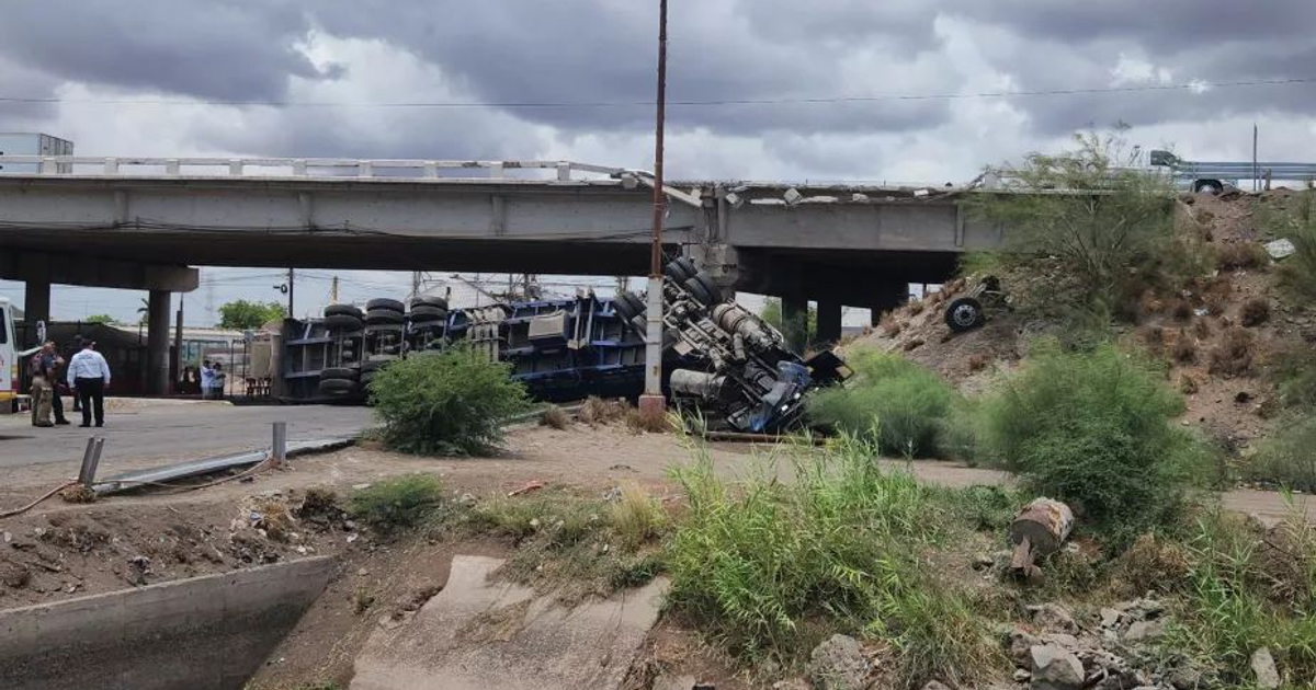 Camión volcado en accidente de tráfico bajo un puente en la carretera Internacional México 15, con cielo nublado y personas alrededor.