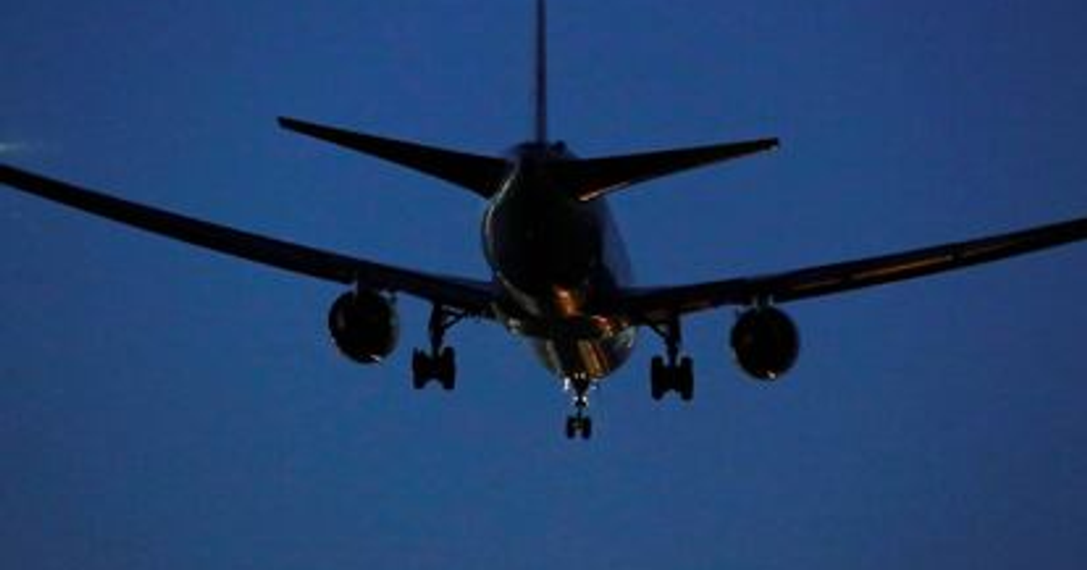 Avión en vuelo visto desde abajo con tren de aterrizaje visible y cielo oscuro de fondo