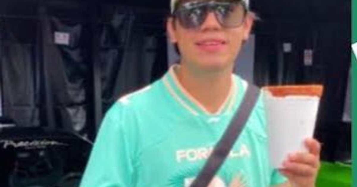 Persona con camiseta aqua y gafas de sol sosteniendo un vaso en un evento nocturno